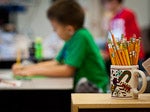 a student working at a desk with a mug full of pencils in the foreground
