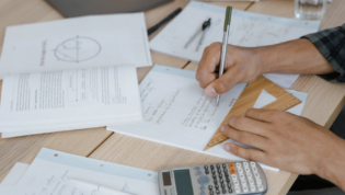 Desk with papers and hand filling out homework
