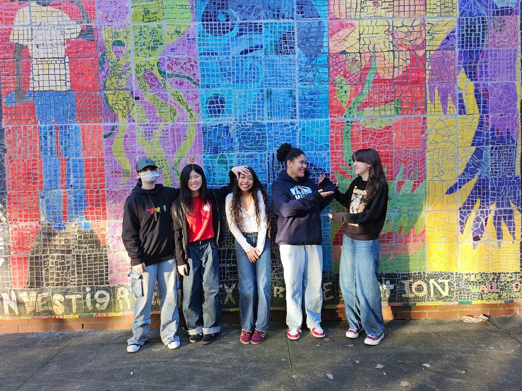 Students standing in front of a mosaic mural 