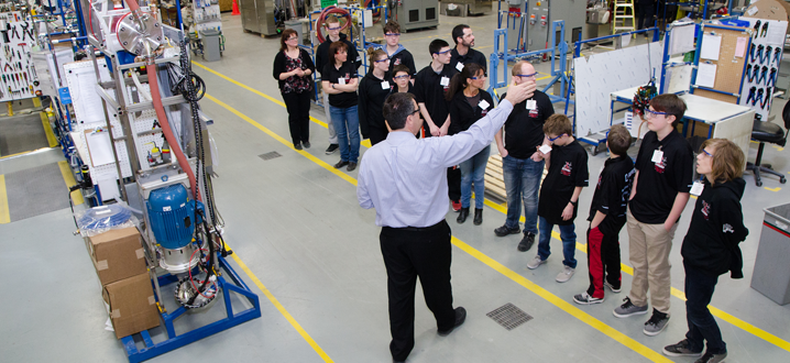 a businessman is pointing out a feature to a group of students on an industry tour