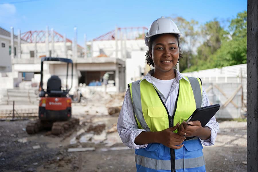 Young African-American Woman in a hard hat and safety vest holding a clipboard on an active construction site