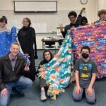 Middle College Students and teacher, Vincent Marx, holding up the tie blankets they made for the parent education lab children