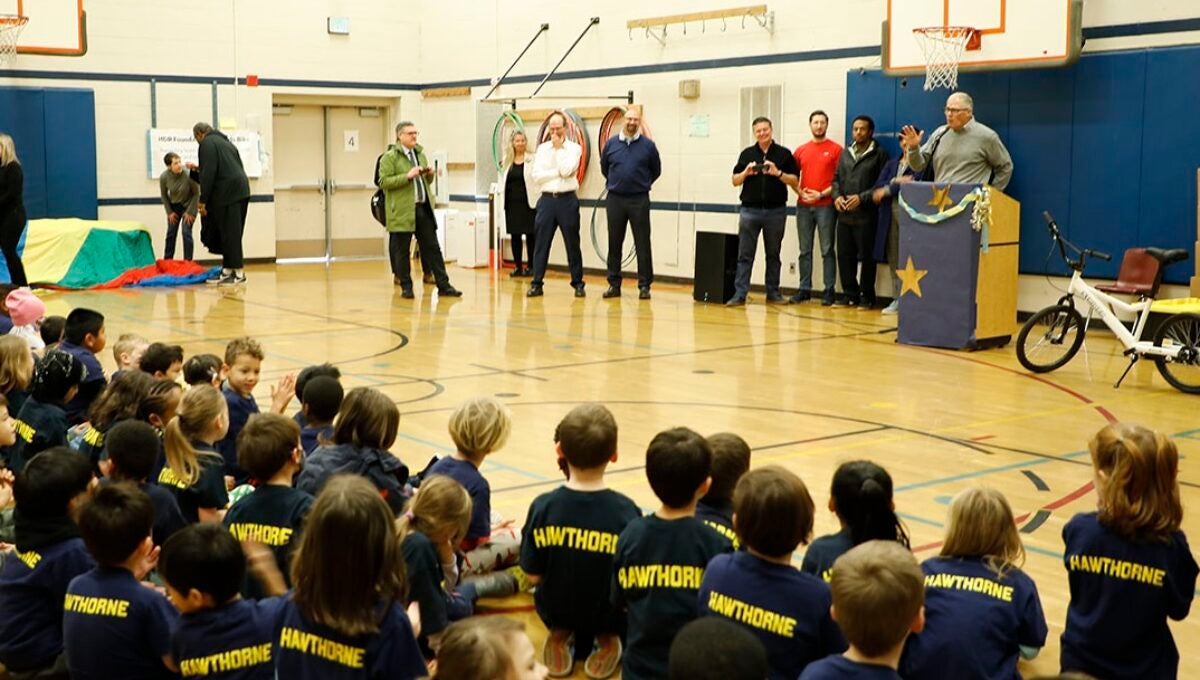 Governor Inslee stands at a podium in the school gym with teachers, school staff and students listening