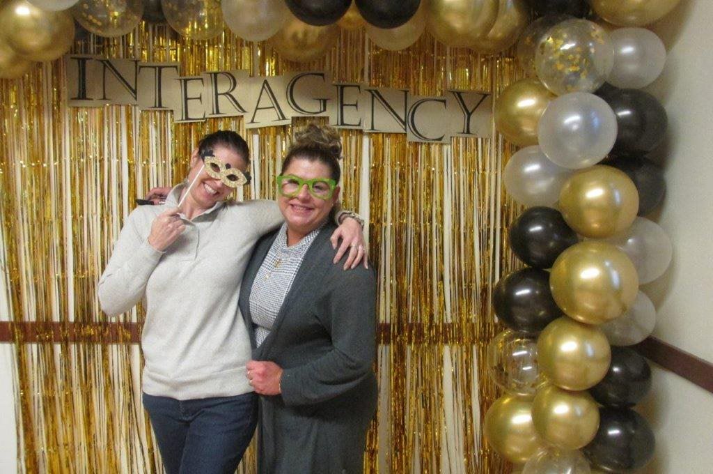 Debbie and Shaylyn pose in front of balloons and Interagency sign