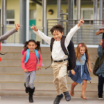Young kids exiting a school, happy and jumping.
