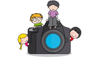 Four smiling children surrounding a camera.