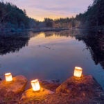 Paper bag luminarias on boulders in front of a dark pond.