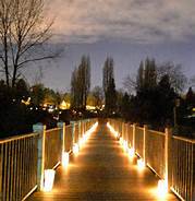 A boardwalk over a pond, with paper bag luminarias lining the walkway.