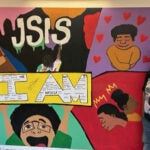 A young man stands beside the mural he painted at school