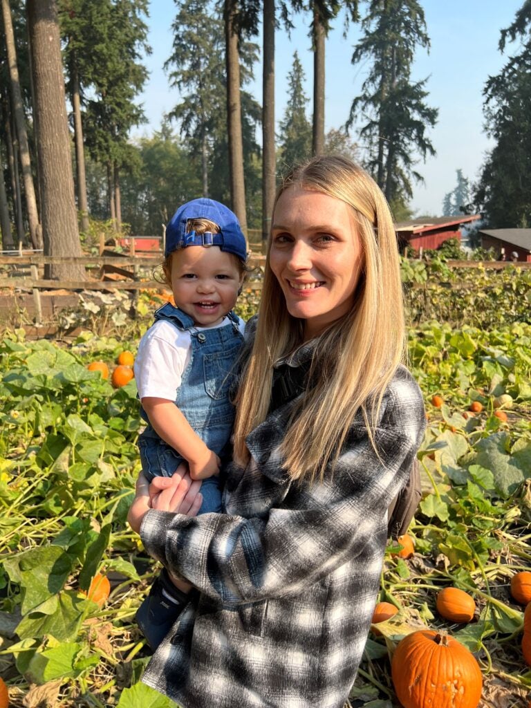 Image of Brittni Zackery standing in a pumpkin patch holding a child 