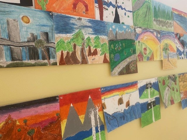 hallway view of works Students learned about creating depth through foreground, middle ground and background and overlapping shapes.