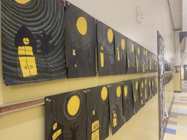 wall view of many cut paper and pastels used to create landscape of houses and the moon.