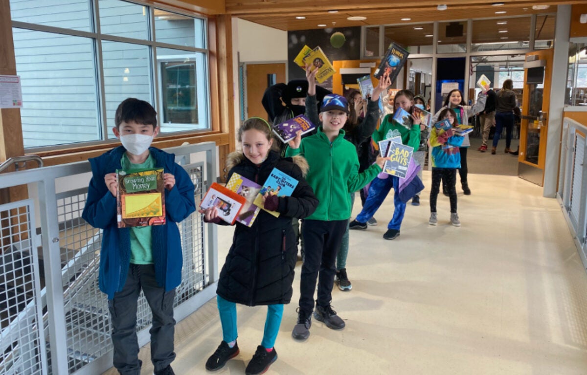group of students holding up their library books outside the school library