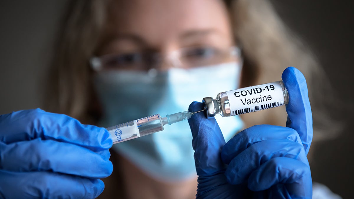 a masked person preparing a covid-19 vaccine