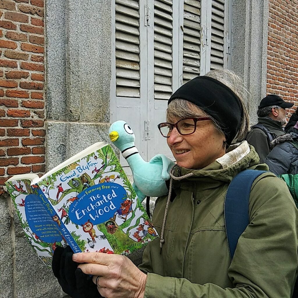 Mrs. Finnegan reading a book with Pigeon on her shoulder.