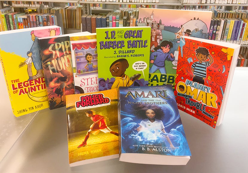 The 2023 global reading challenge books arrange on the table. They include The legend of Auntie Po, Spirit Hunters Island of the Monsters, Stef Soto Taco Queen, JD and the Great Barber Battle, Rabbit Chase, Planet Omar Trouble Magnet, Power Forward, and Amari and the Night Brothers.