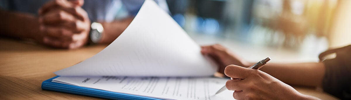 Hand and pen completing paperwork at desk banner