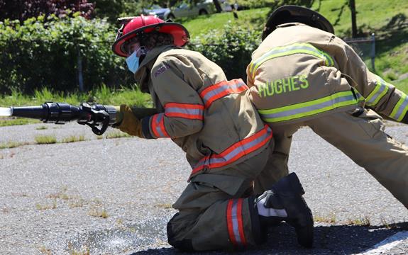 2 students in firefighter gear folding a firehose