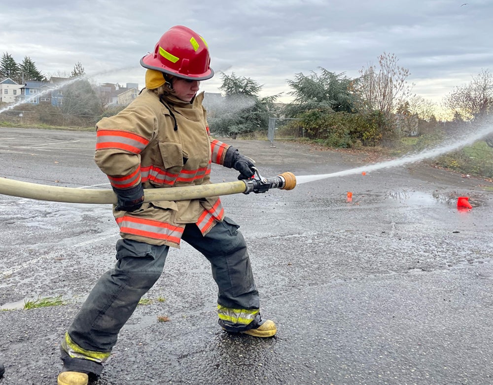 A student in firefighter gear holds a water hose during a training