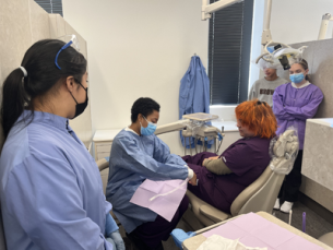 Students standing in dentist office simulation classroom practicing bedside manner skills