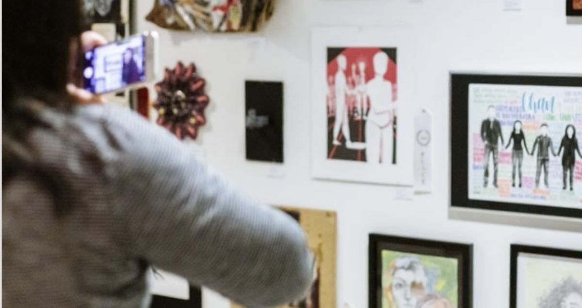 Person talking a photo of artwork on the wall. Photo from the Seattle Art Museum promotion of the event.