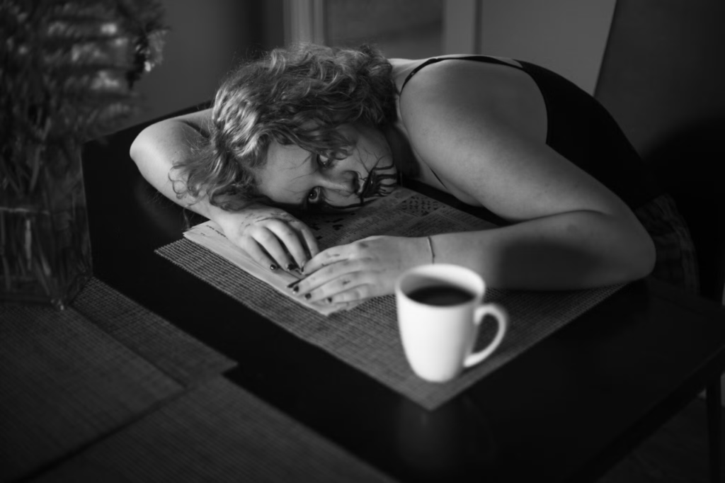 Person with head on table and coffee cup. Lake Neil: Grade 12, “Poison”