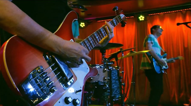 Close up of Guitar and hand playing and singers in background. Letters to Melissa Film.