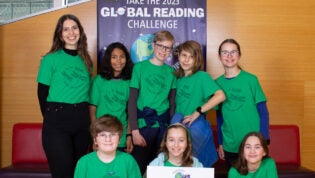 A group of students and a teacher gather for a photo in front of library Global Reading Challenge banner.